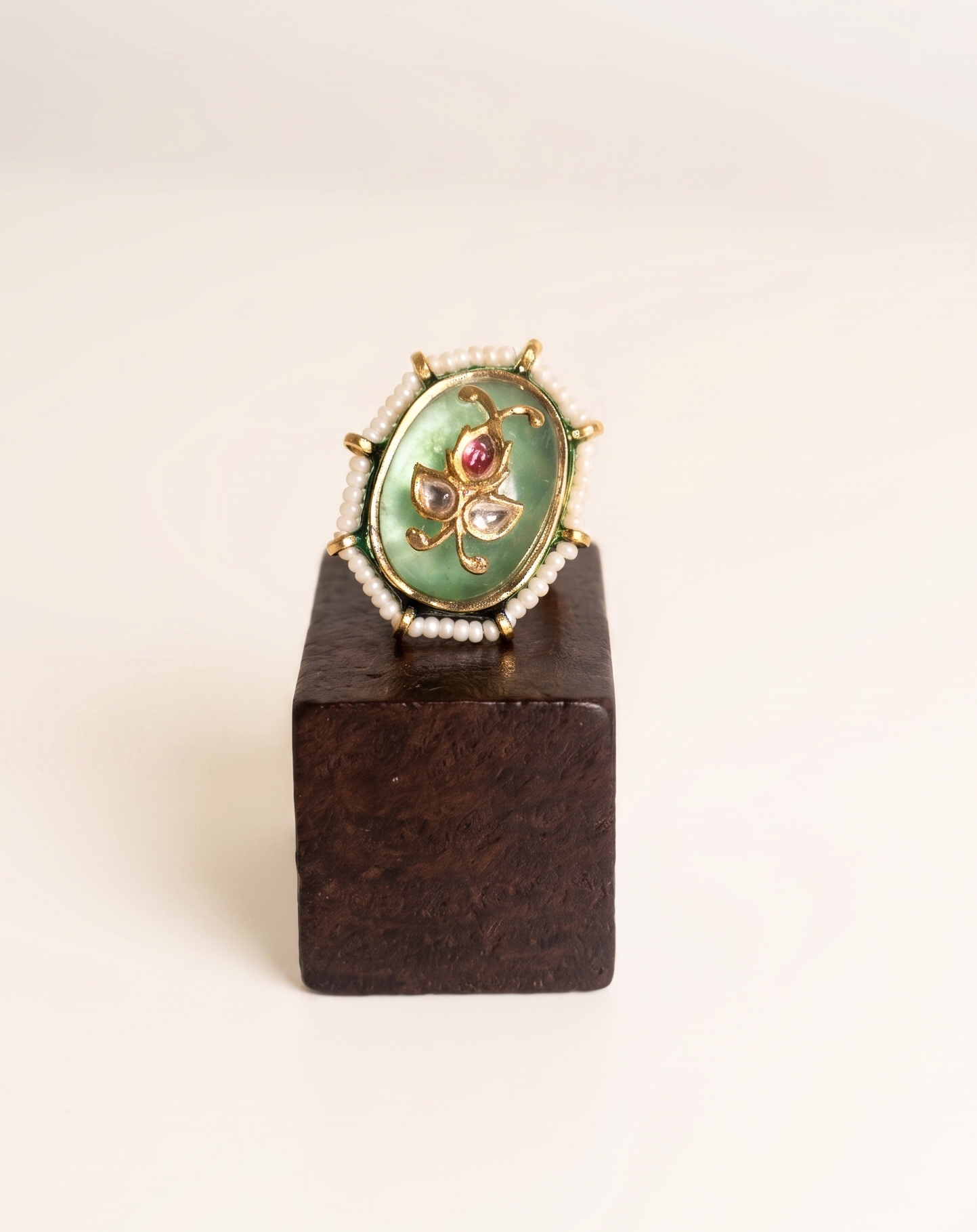Decorative ring with green gemstone and gold accents on a wooden stand against a white background