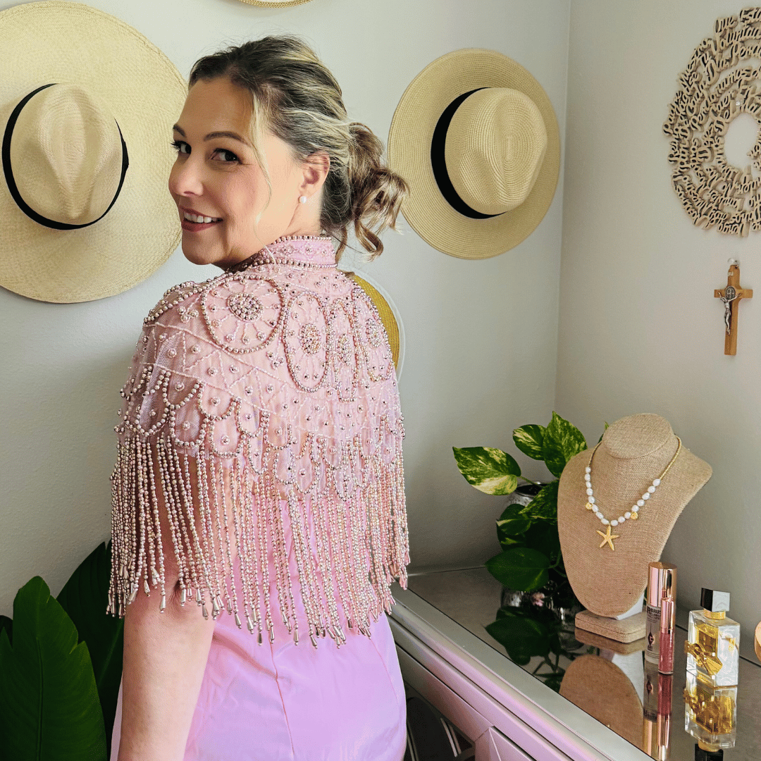 Woman wearing a pink beaded top in a room with hats and jewelry on display.