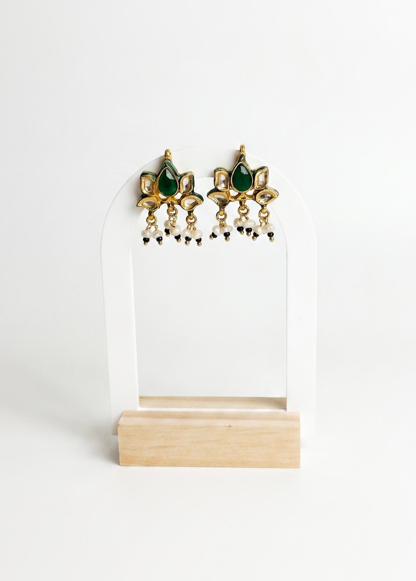 Pair of gold and green earrings on a white stand with a white background