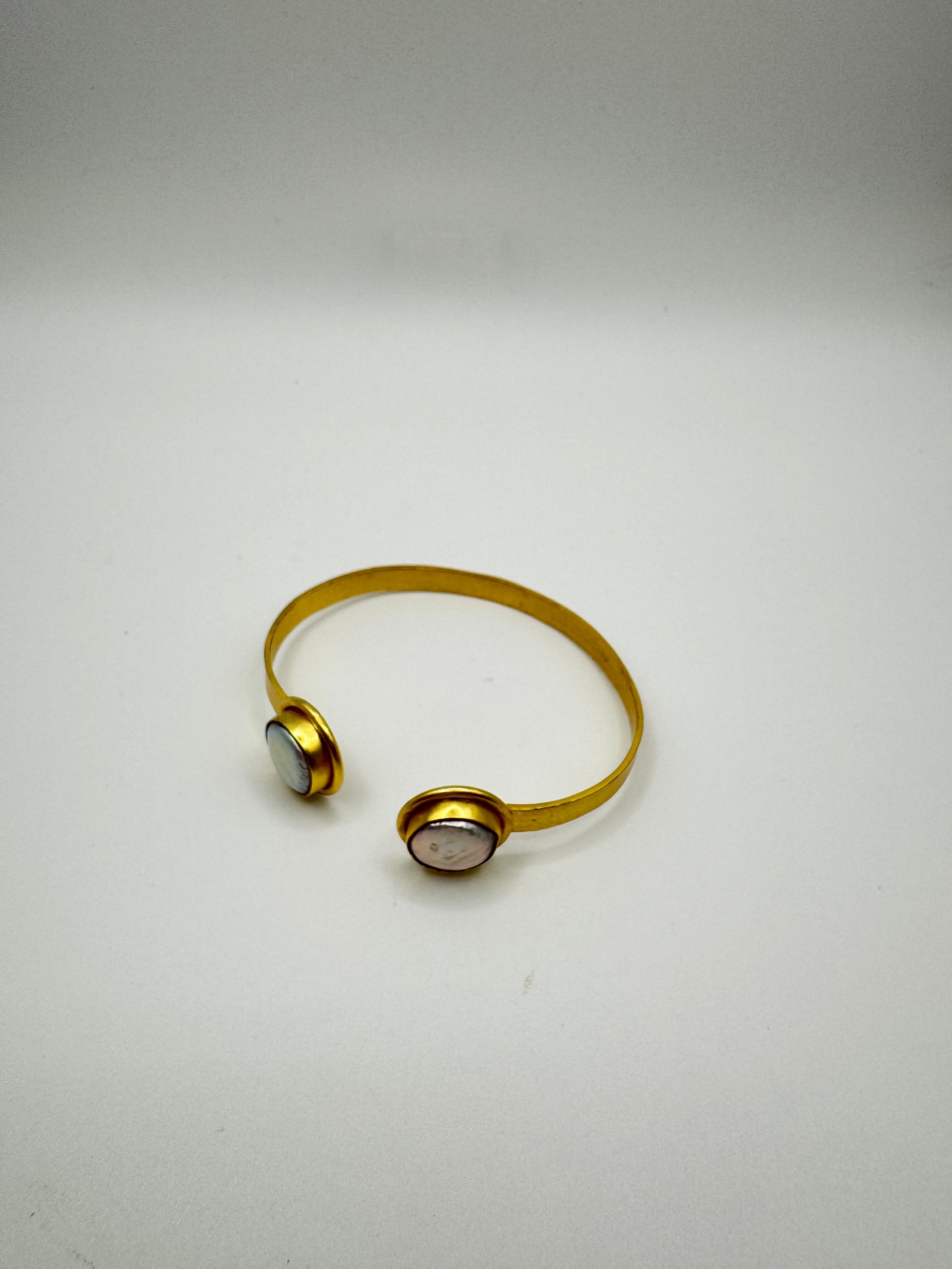 Gold bracelet with two circular ends on a light gray background
