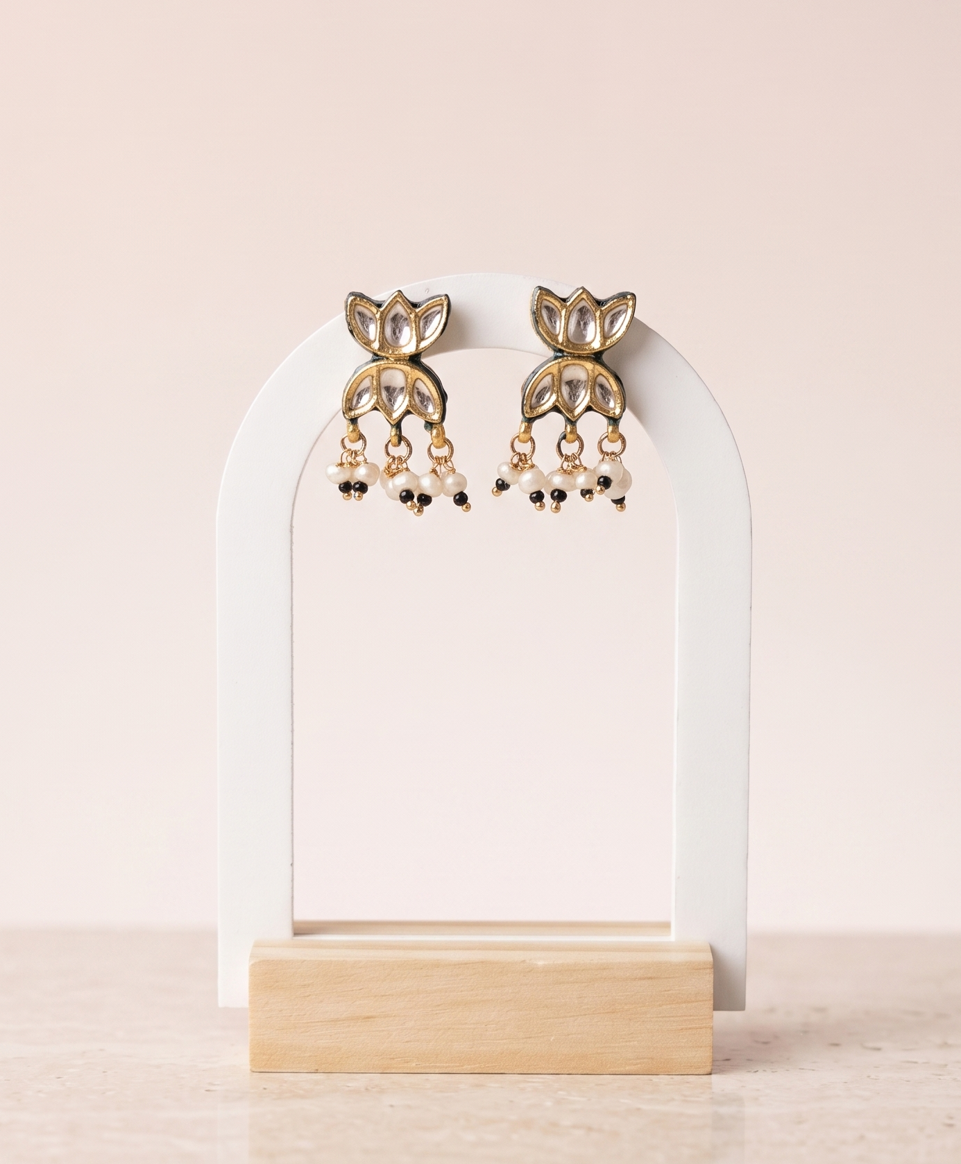 Gold earrings on a white arch stand with a beige background