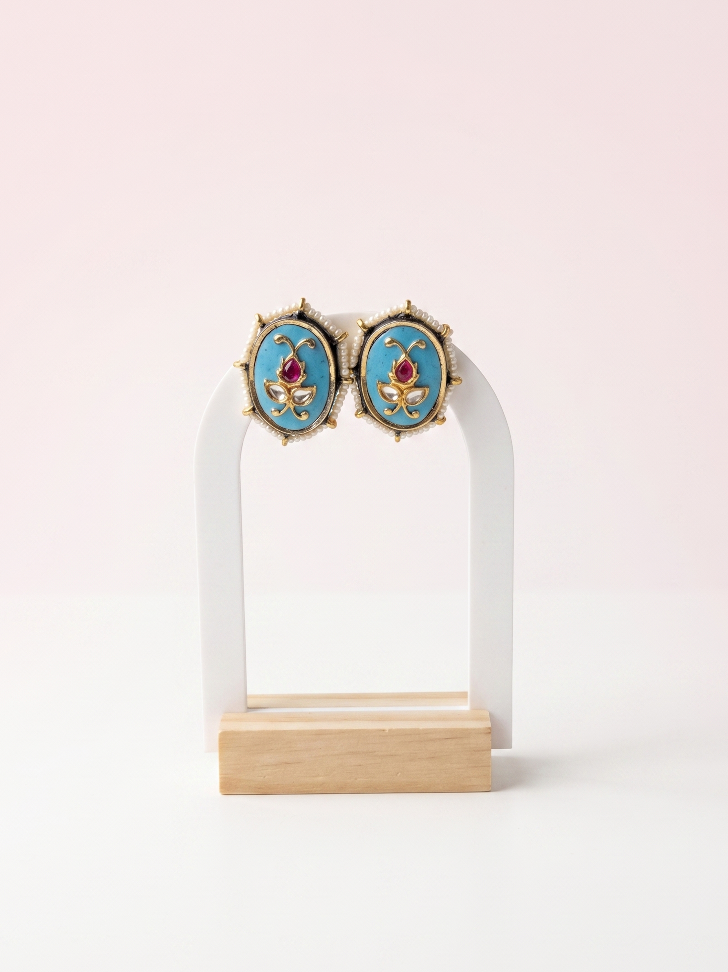 Pair of earrings on a white stand with a light pink background