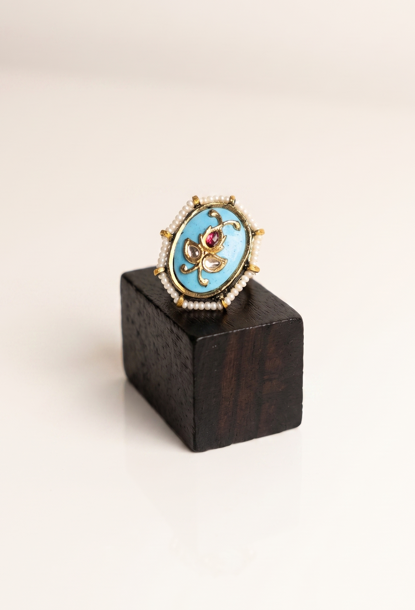 Decorative ring with a blue stone and gold accents on a wooden stand against a white background