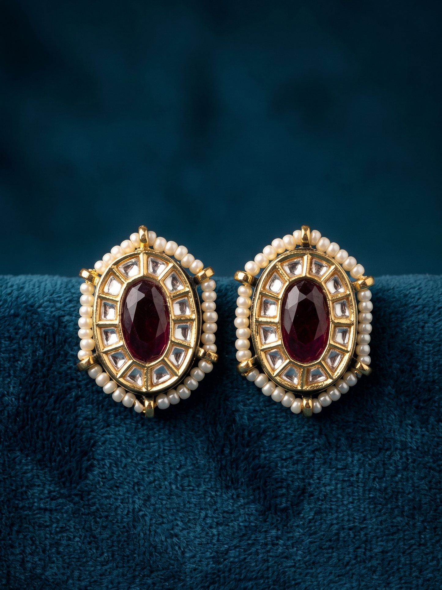 Pair of gold earrings with red gemstones on a blue background