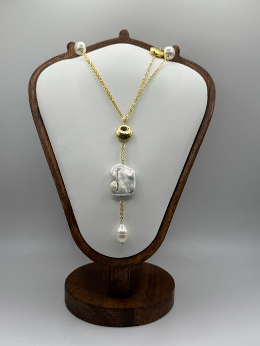 Gold necklace with pearls on a wooden display stand against a gray background