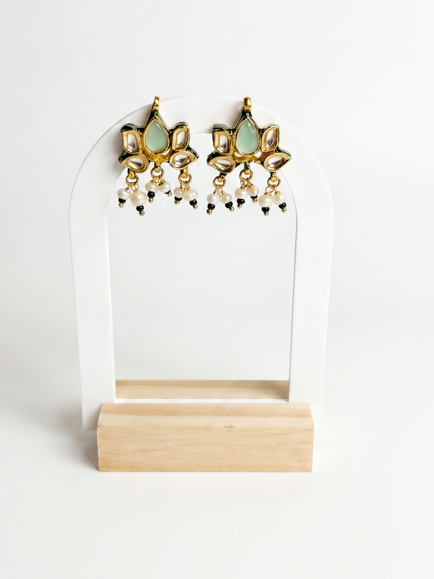 Pair of gold and green earrings on a white stand with a wooden base.