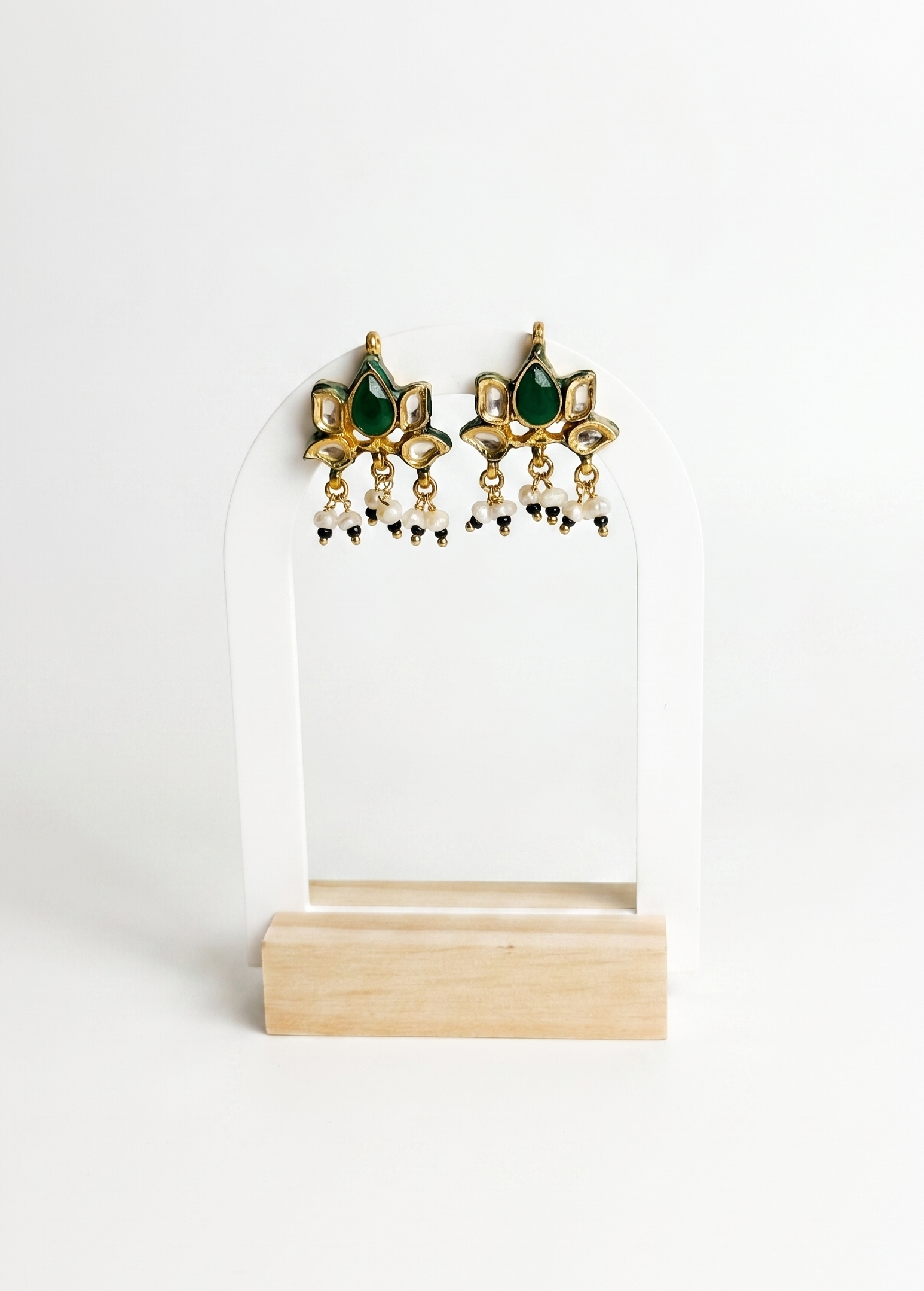 Pair of gold and green earrings on a white stand with a white background