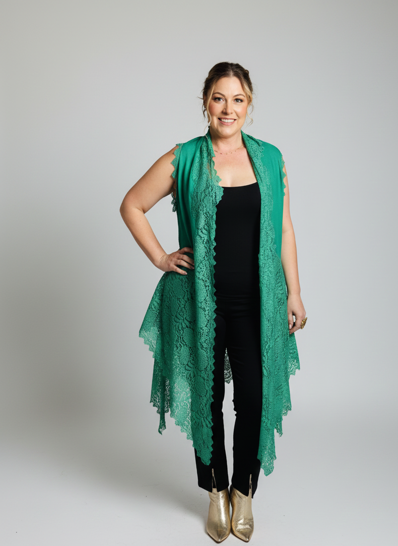 Woman wearing a green lace vest over a black top and pants on a gray background