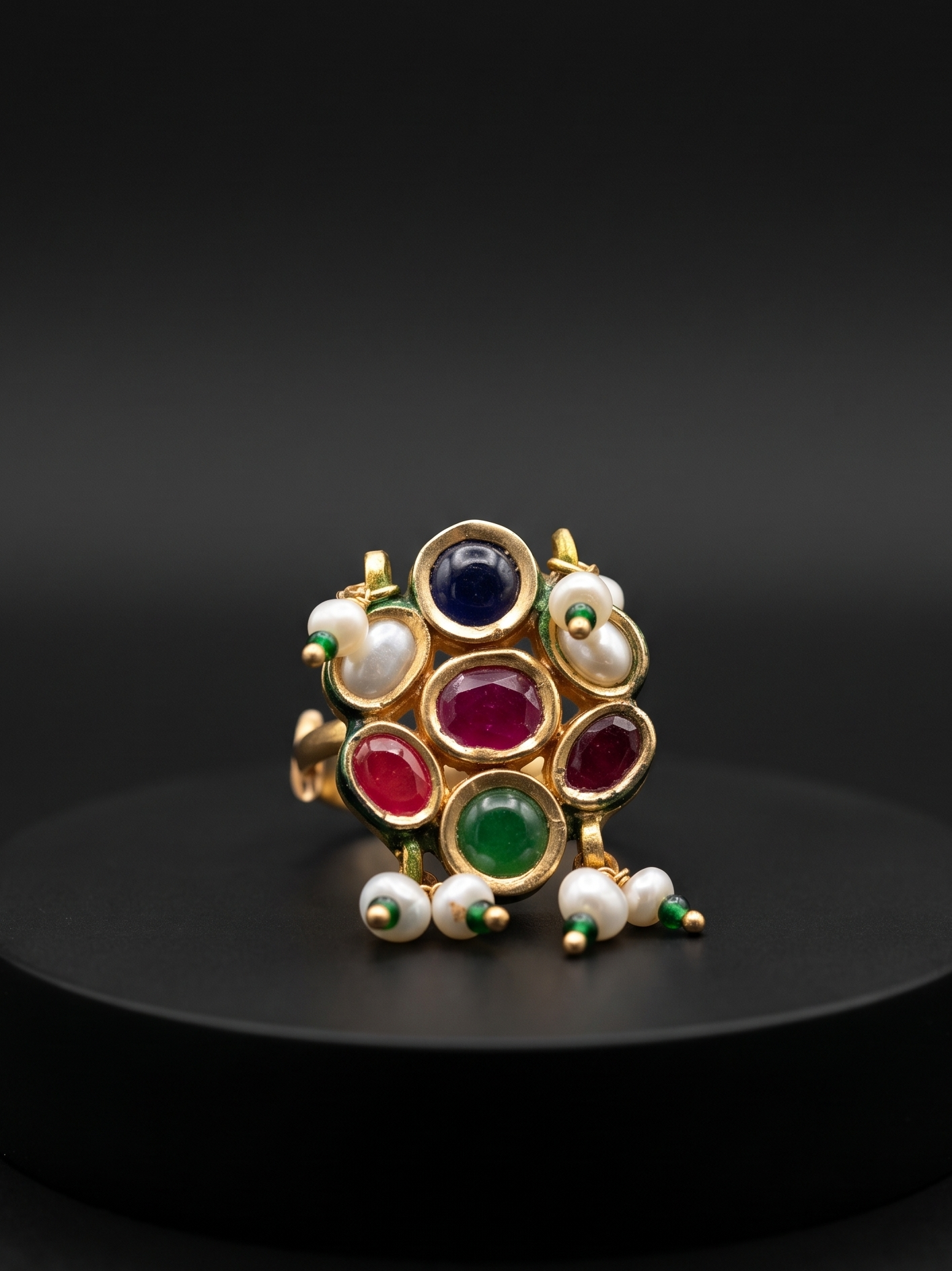 Decorative ring with colored stones and pearls on a black pedestal against a dark background