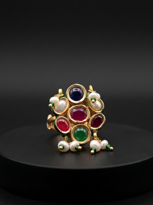 Decorative ring with colored stones and pearls on a black pedestal against a dark background