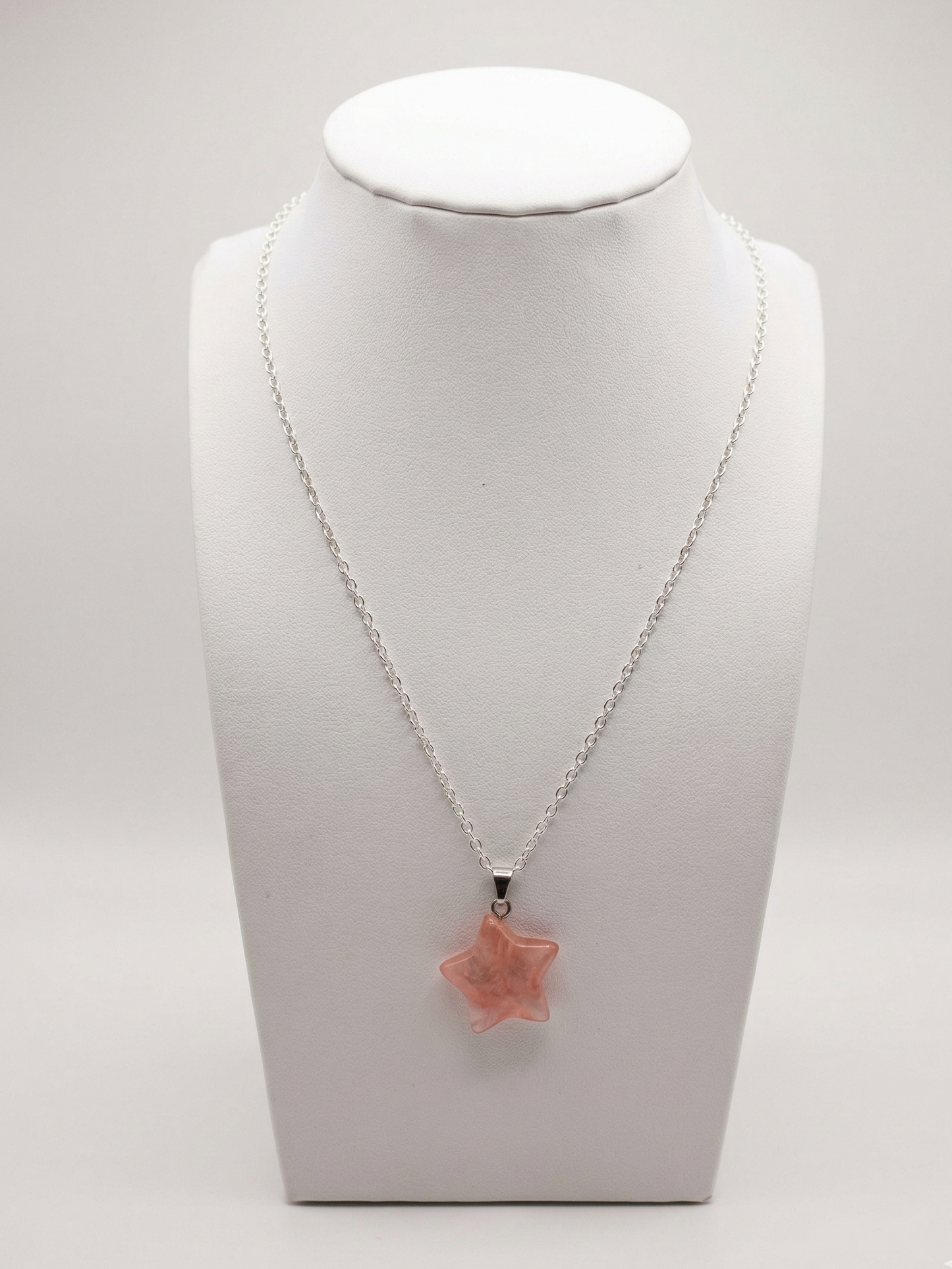Necklace with a star-shaped pink pendant on a white mannequin bust.