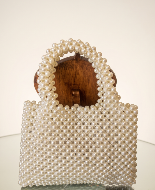 Pearl-handled handbag on a reflective surface with a neutral background