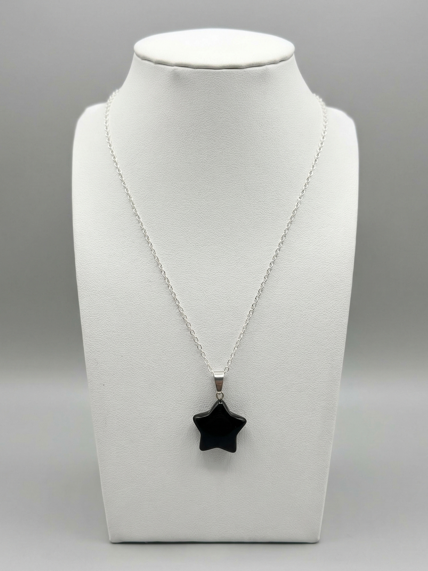 Necklace with a black star pendant on a white mannequin bust against a gray background