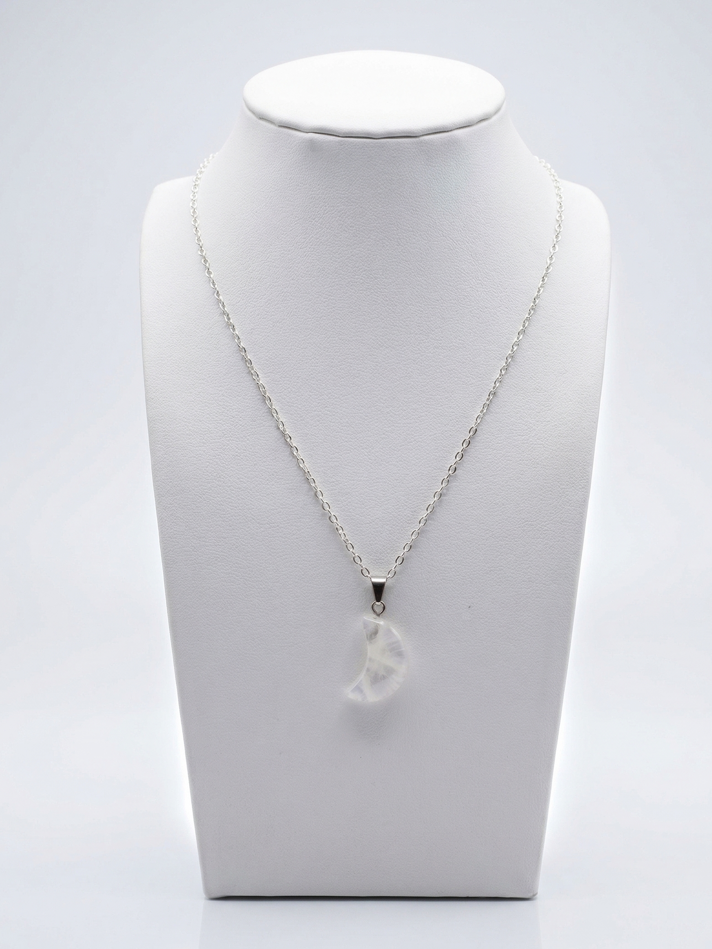 Silver necklace with a clear pendant on a white mannequin bust against a light gray background
