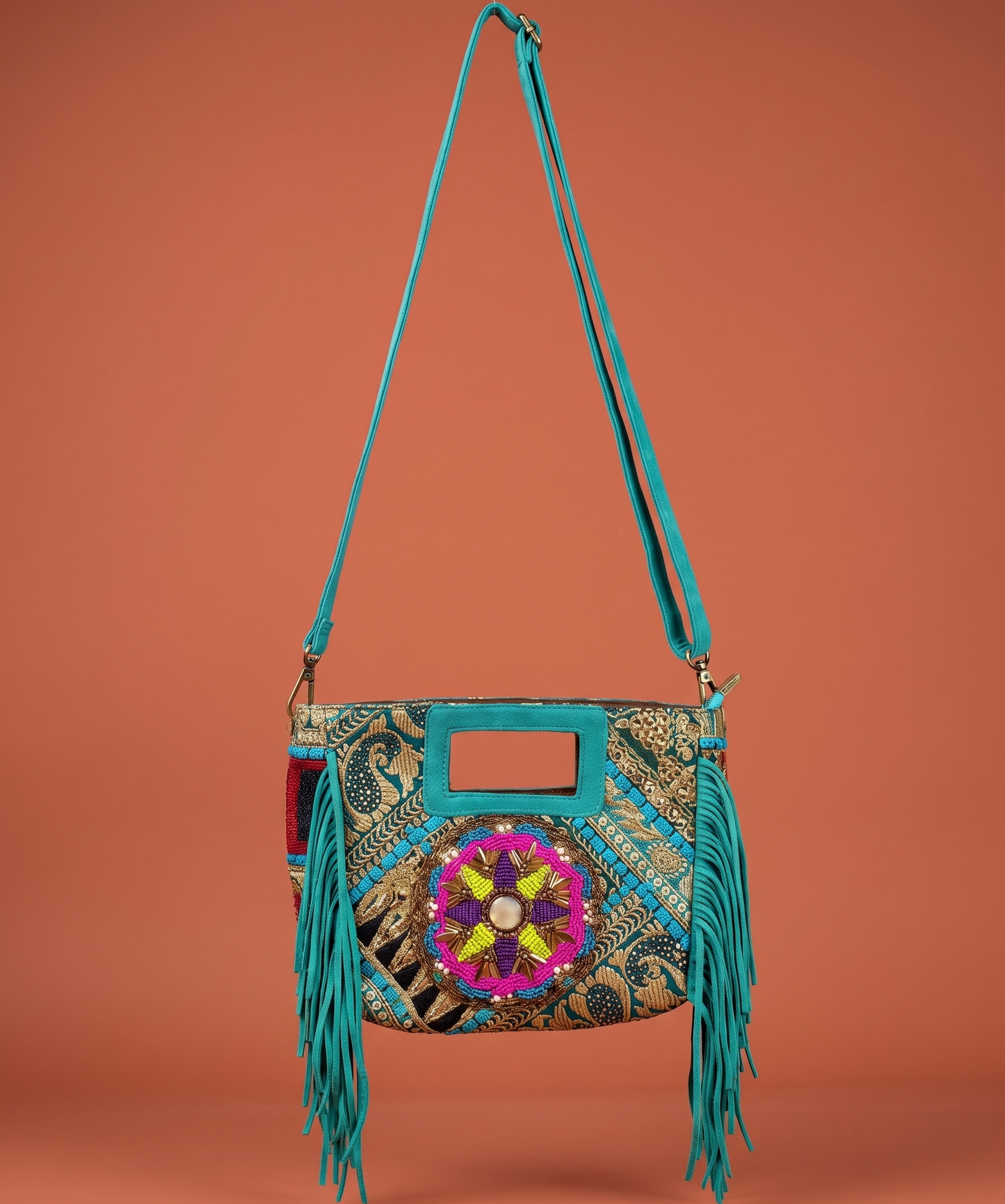 Turquoise handbag with colorful floral design and fringes on an orange background