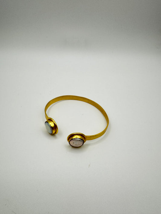 Gold bracelet with two circular ends on a light gray background