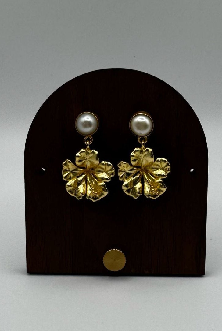 Pair of gold and pearl earrings on a black earring stand against a gray background