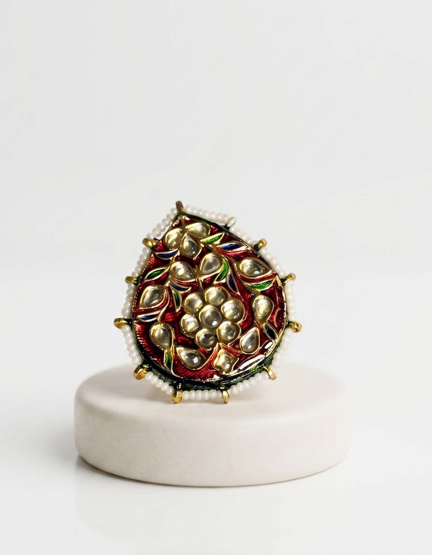 Decorative ring with pearl-like stones on a white pedestal against a white background