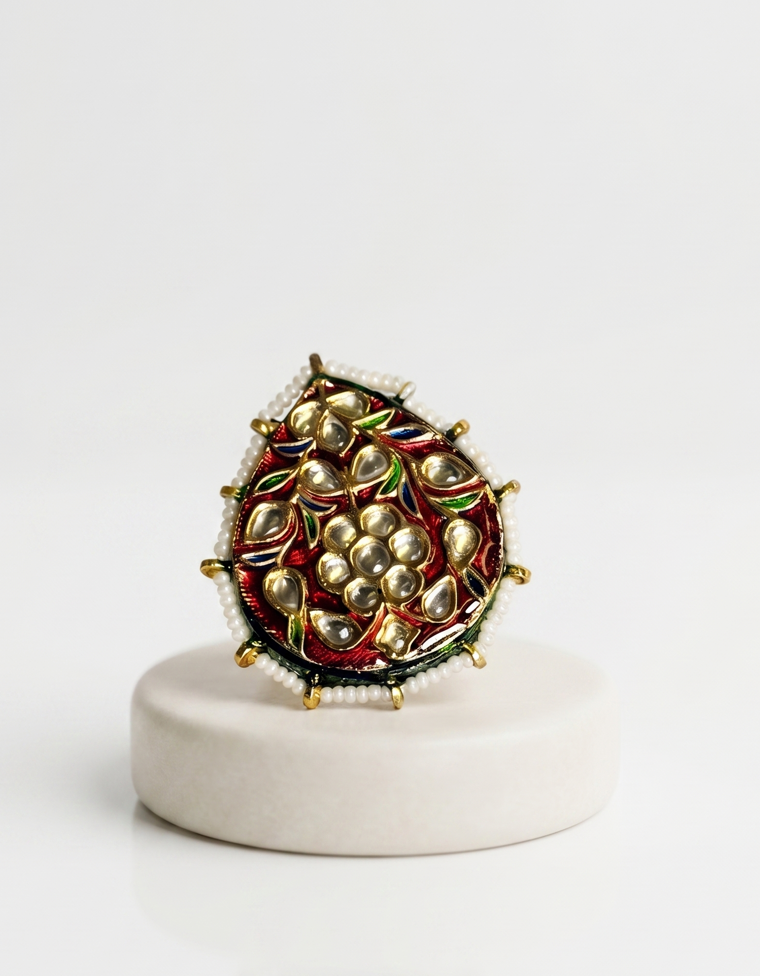 Decorative ring with pearl-like stones on a white pedestal against a white background