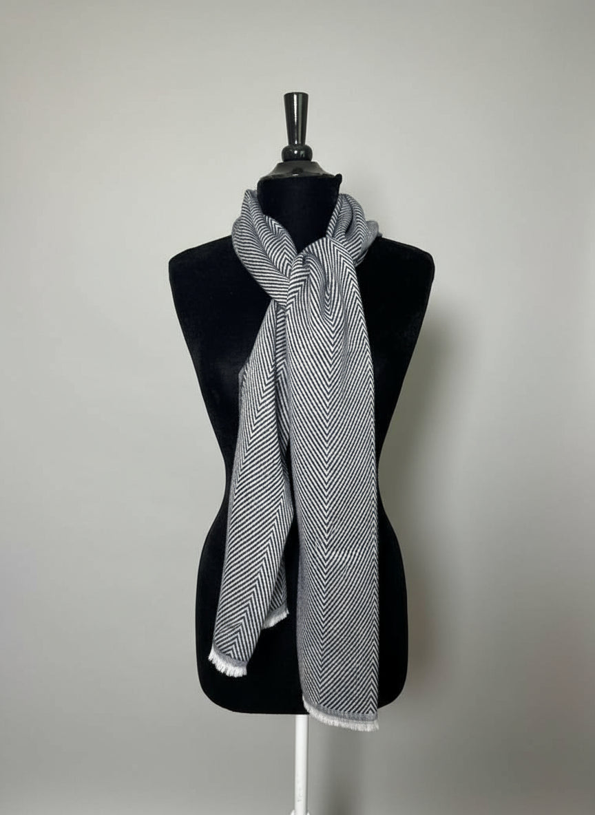 Mannequin wearing a black and white striped scarf with a hat and jewelry on a cabinet in the background.