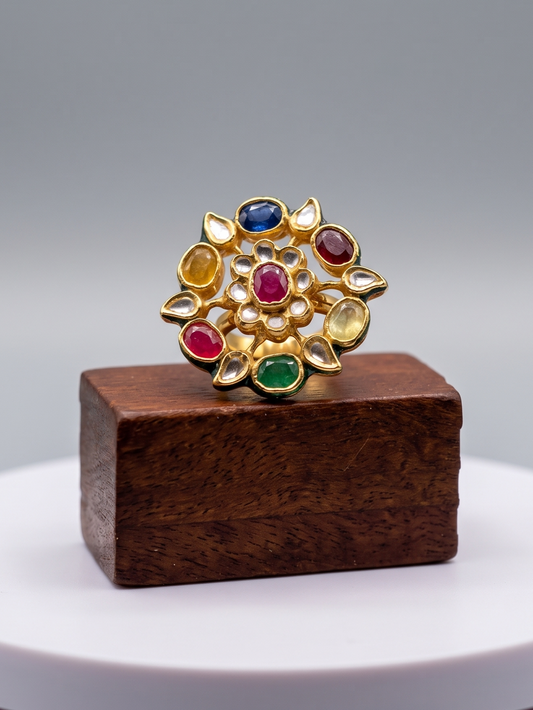 Gold ring with colorful gemstones on a wooden stand against a gray background