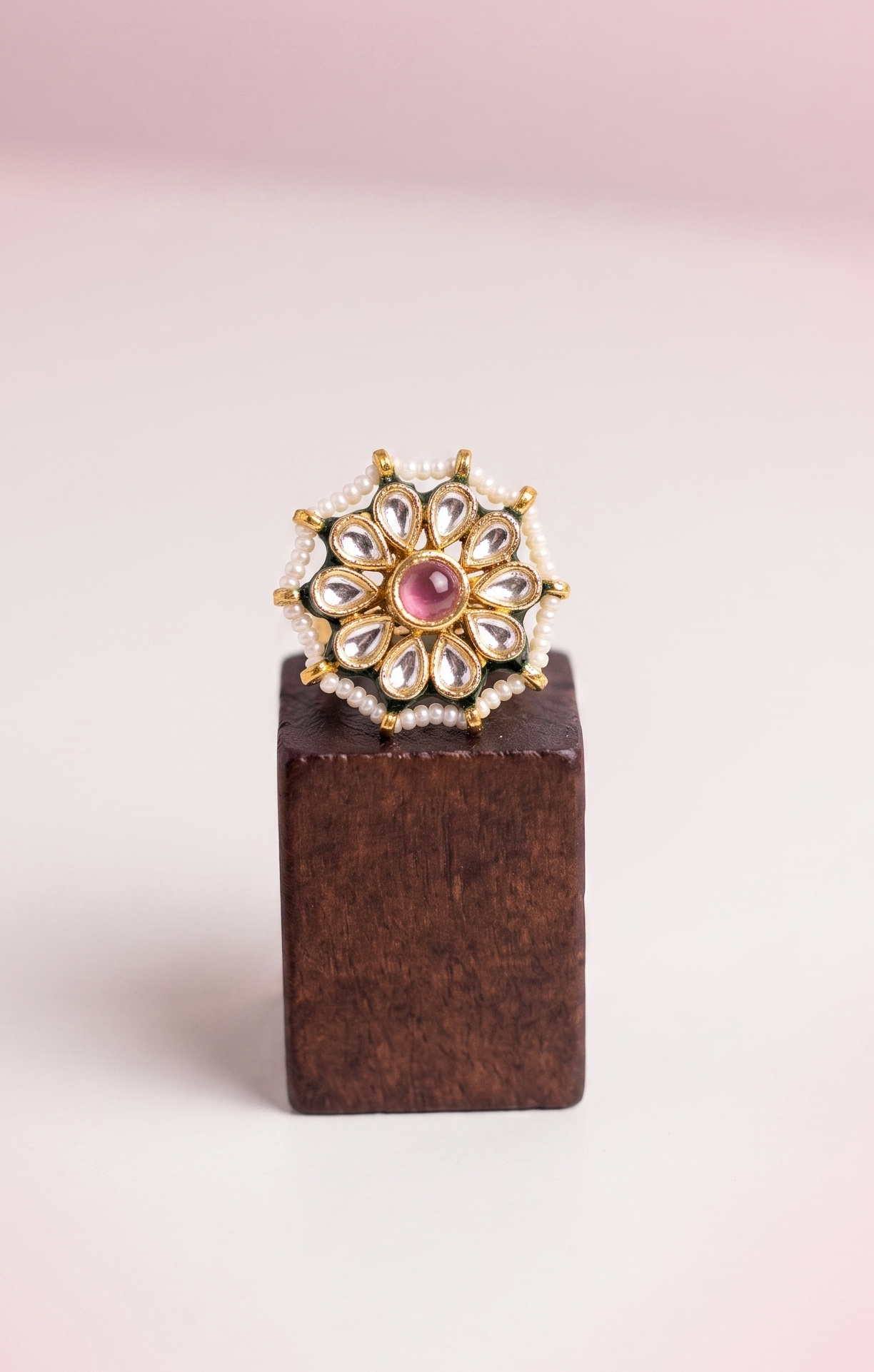 Jewelry ring with pink gemstone on a wooden block against a light pink background