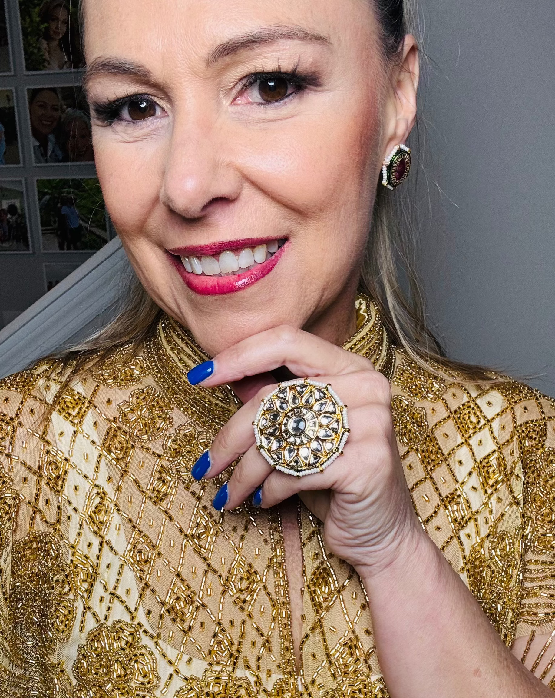 Woman wearing a gold beaded top with a large ring, smiling.