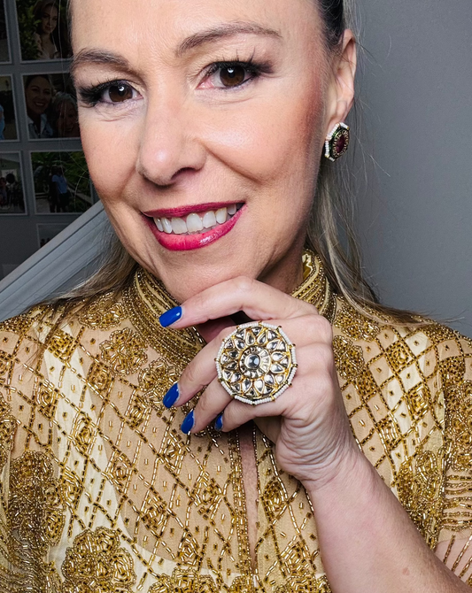 Woman wearing a gold beaded top with a large ring, smiling.