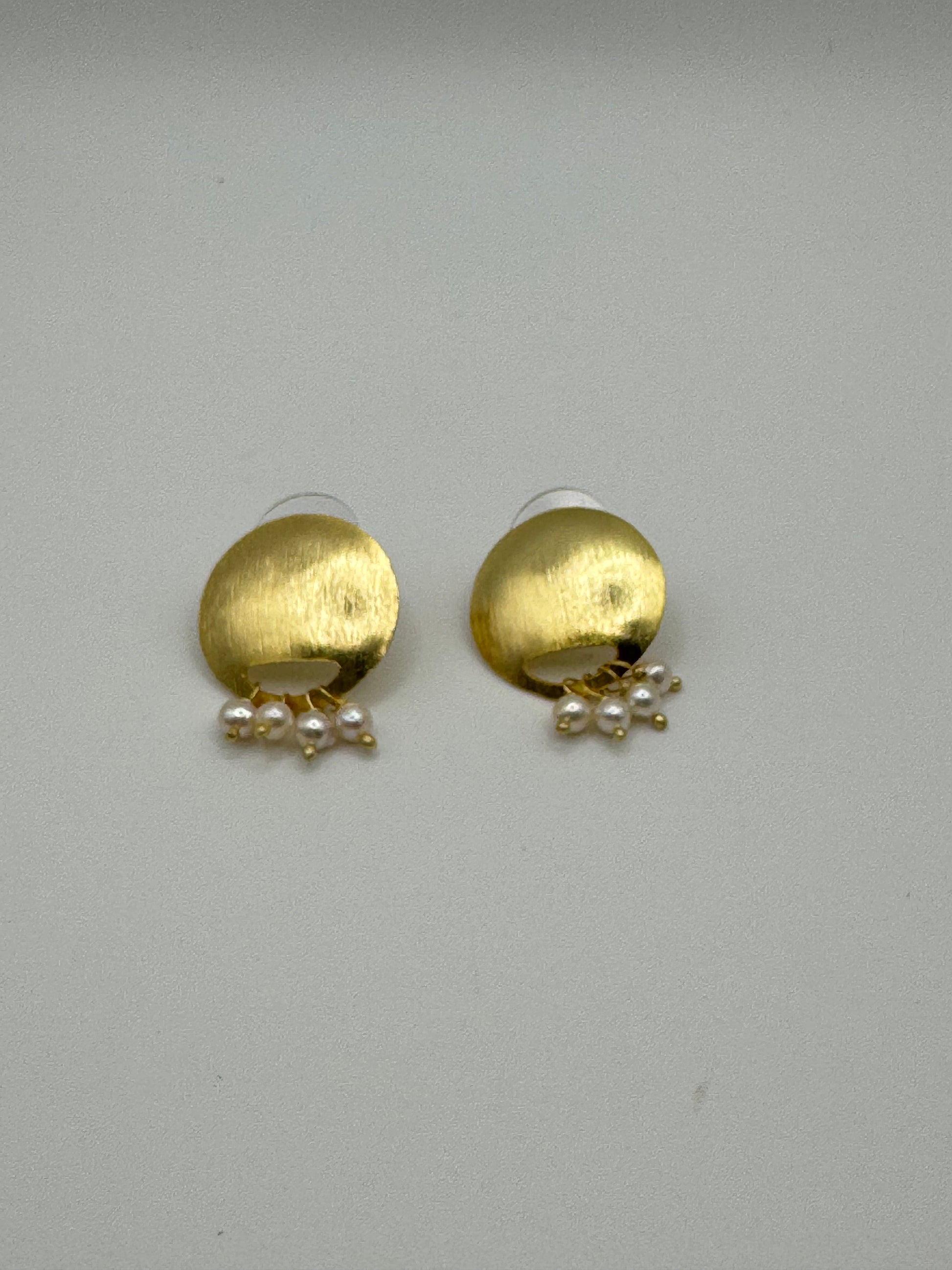 Gold earrings with pearl drops on a light gray background
