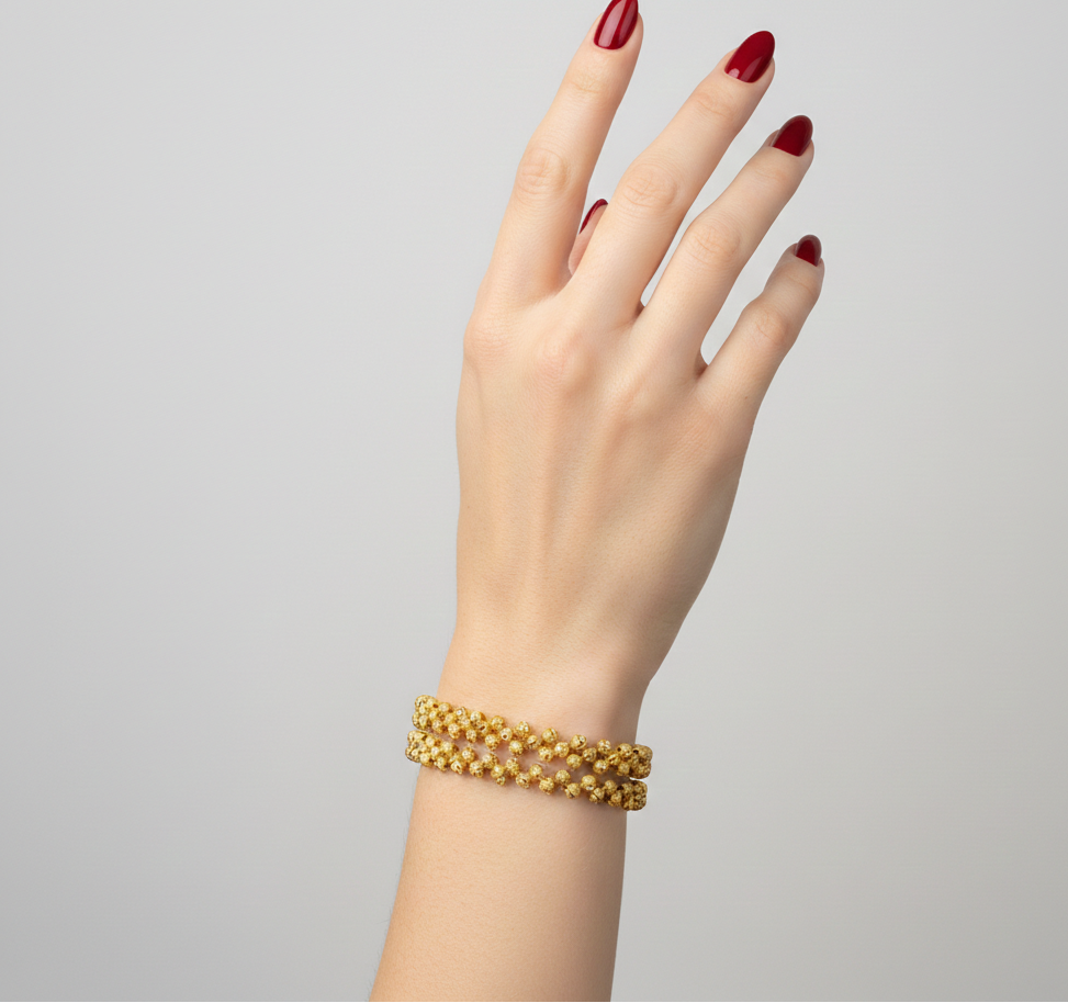 Gold bracelet on a hand with red nail polish against a gray background