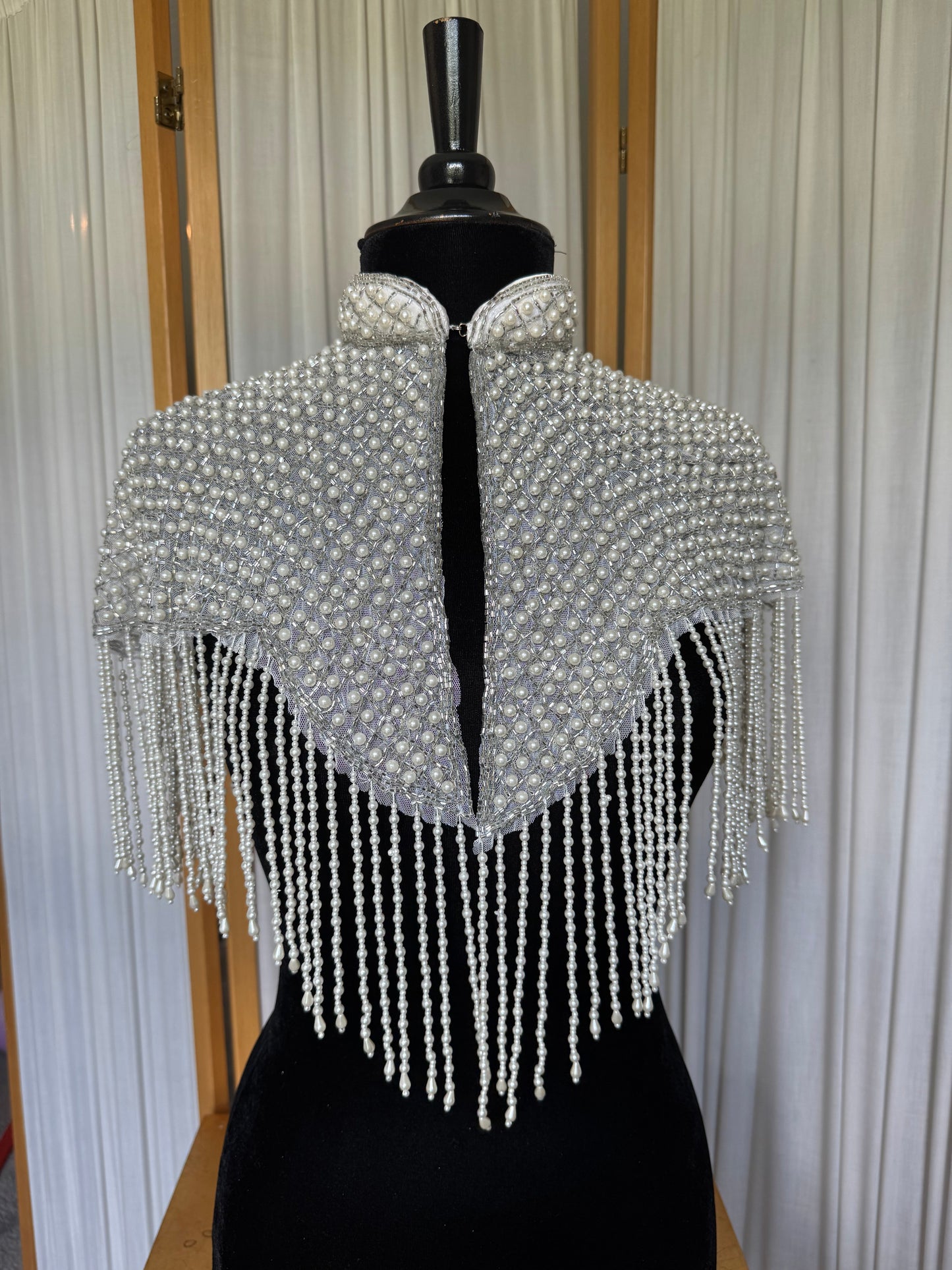 Pearl-studded shawl with fringe on a mannequin against a white curtain background