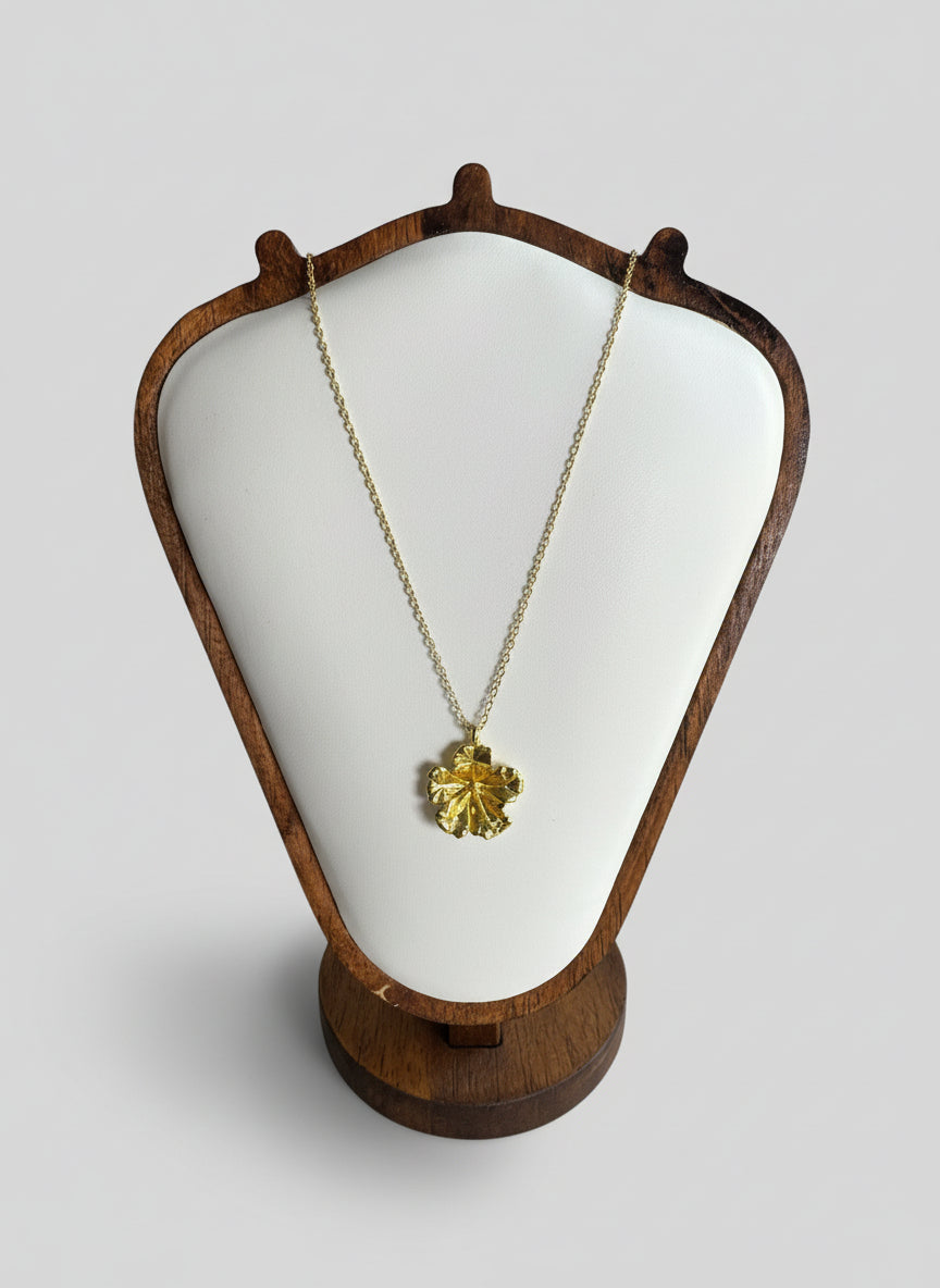 Gold necklace with a leaf pendant on a white cushioned stand against a neutral background