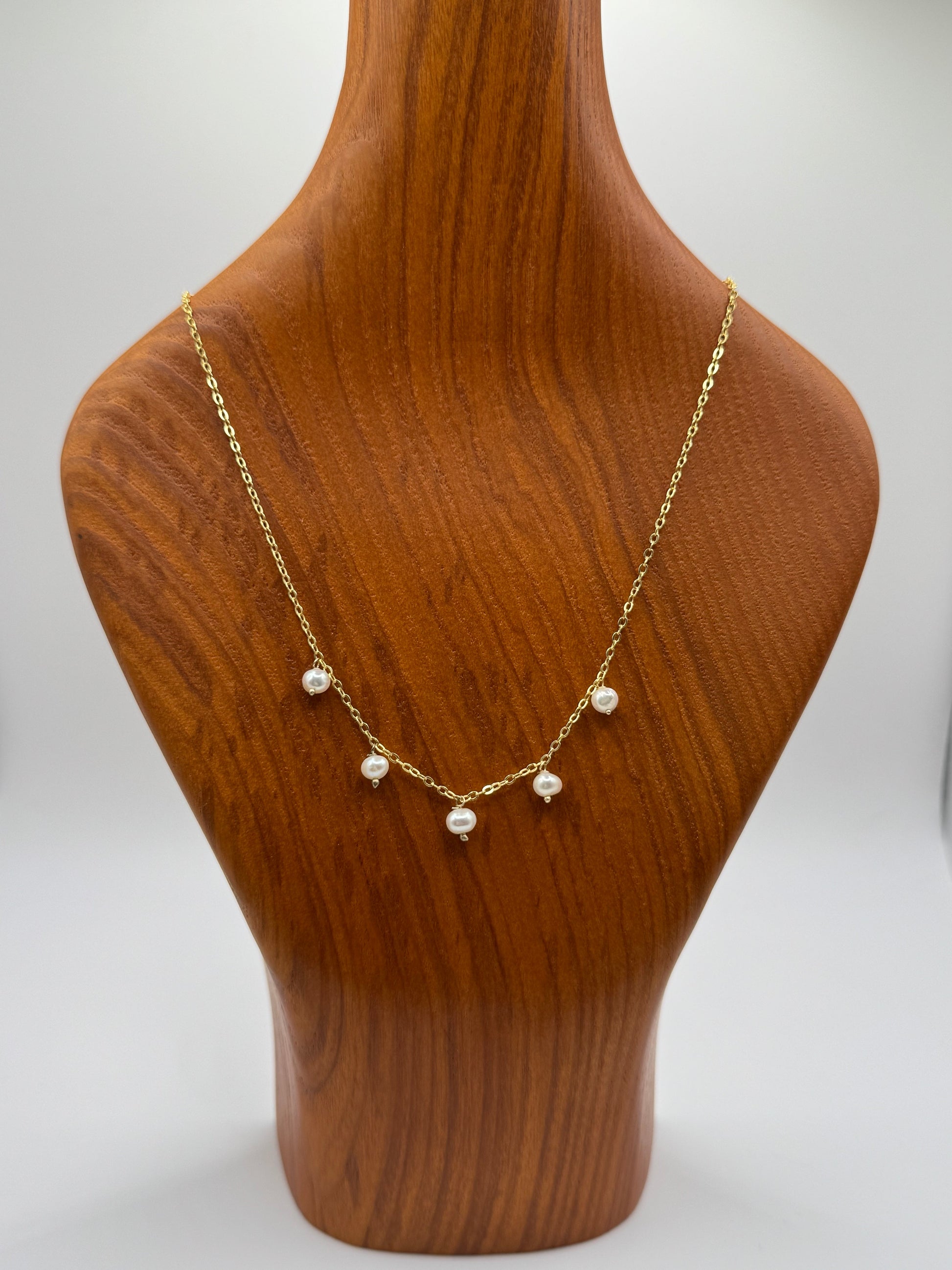 Gold necklace with pearls on a wooden mannequin bust against a white background