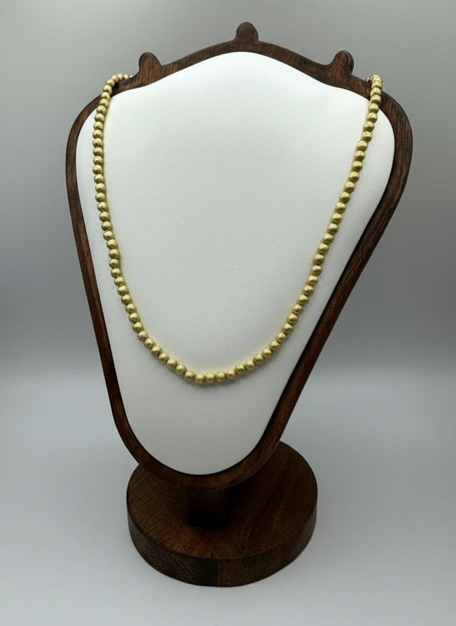 Gold necklace on a wooden display stand against a white background