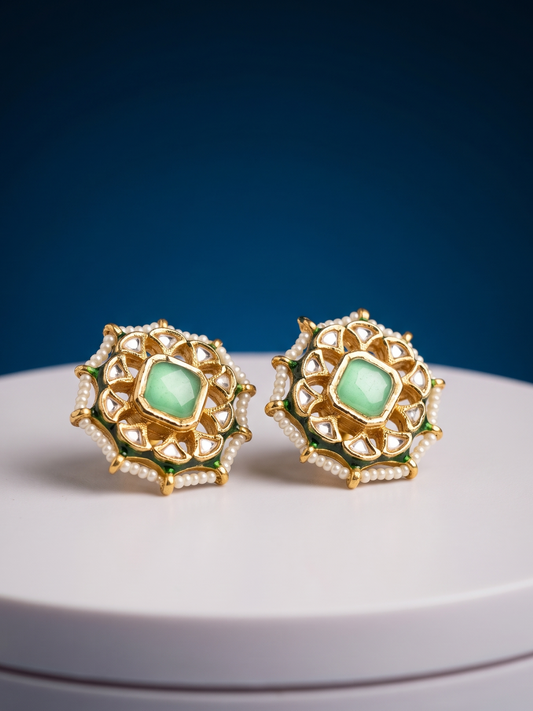 Gold earrings with green gemstones on a white platform against a blue background