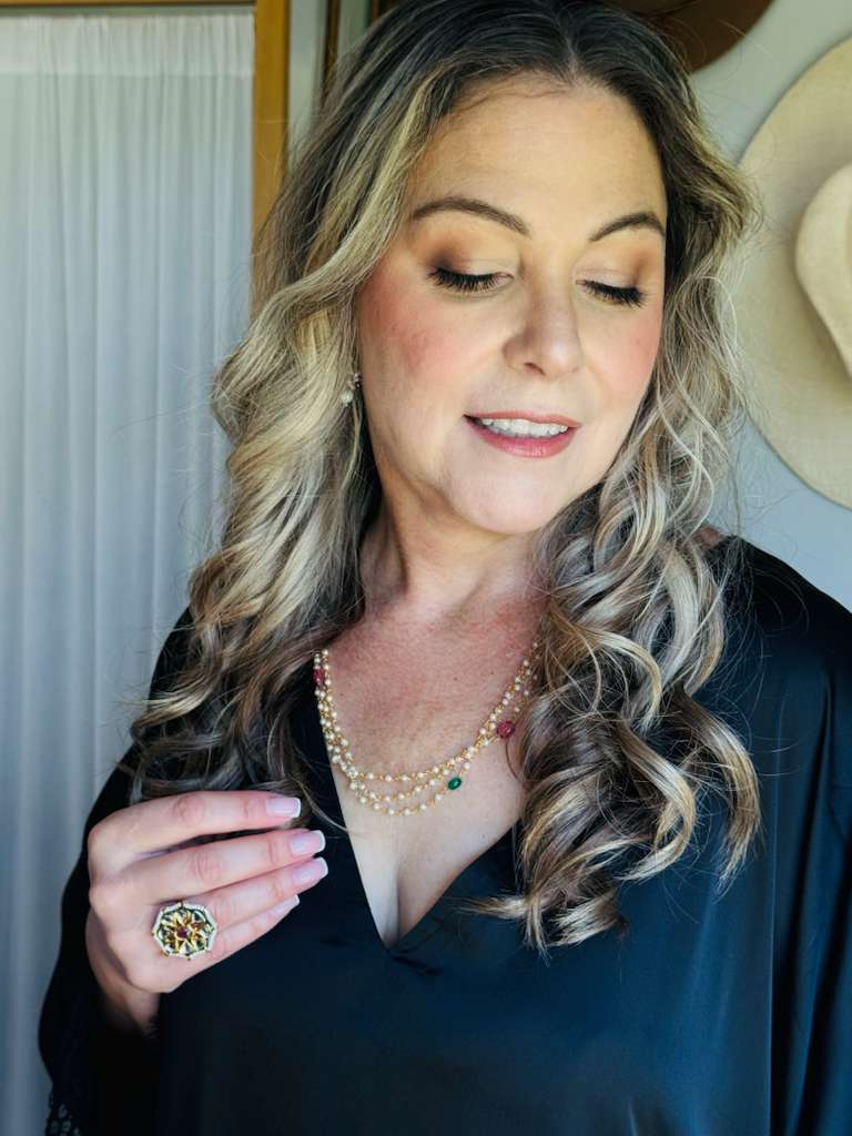 Woman wearing a necklace with a green gemstone, holding it up to her chest.