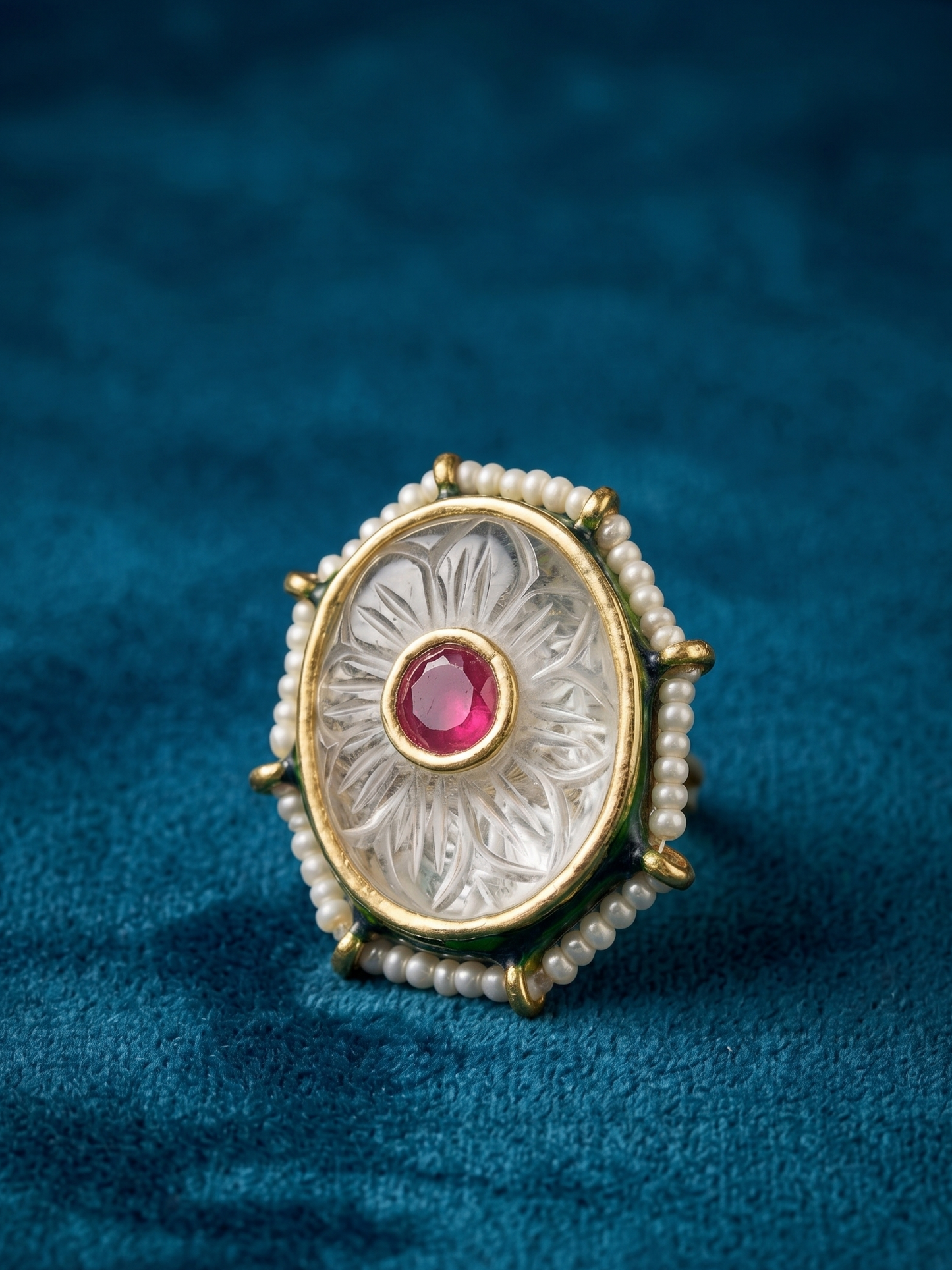 Decorative ring with a red gemstone and pearl accents on a blue fabric background