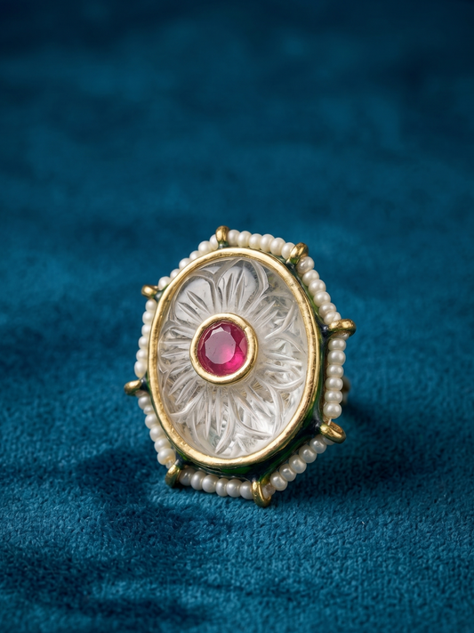 Decorative ring with a red gemstone and pearl accents on a blue fabric background